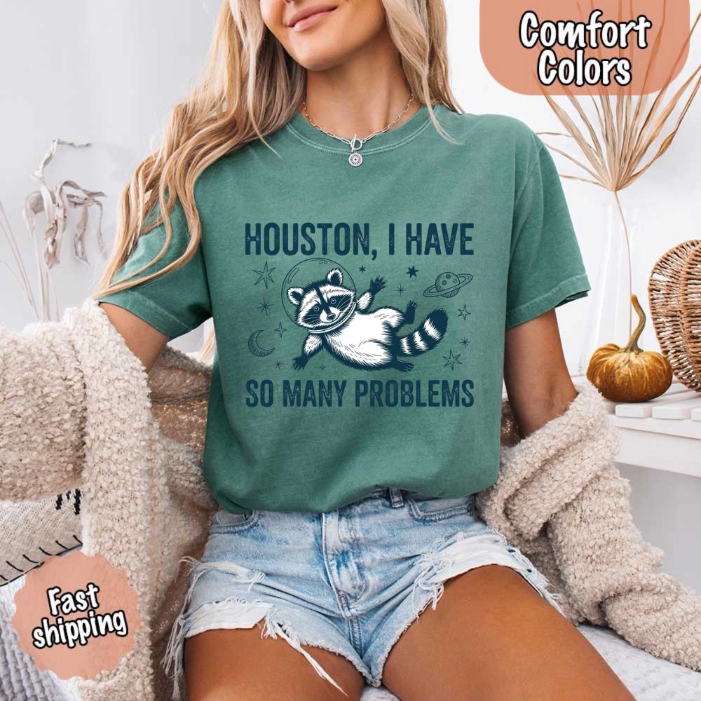 Model wearing Houston I Have So Many Problems Raccoon Comfort Colors T-Shirts, featuring a space-themed raccoon design.