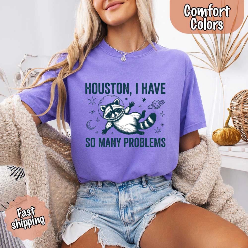 Woman wearing 'Houston I Have So Many Problems Raccoon Comfort Colors T-Shirts' with cartoon raccoon, space-themed design. Fast shipping.