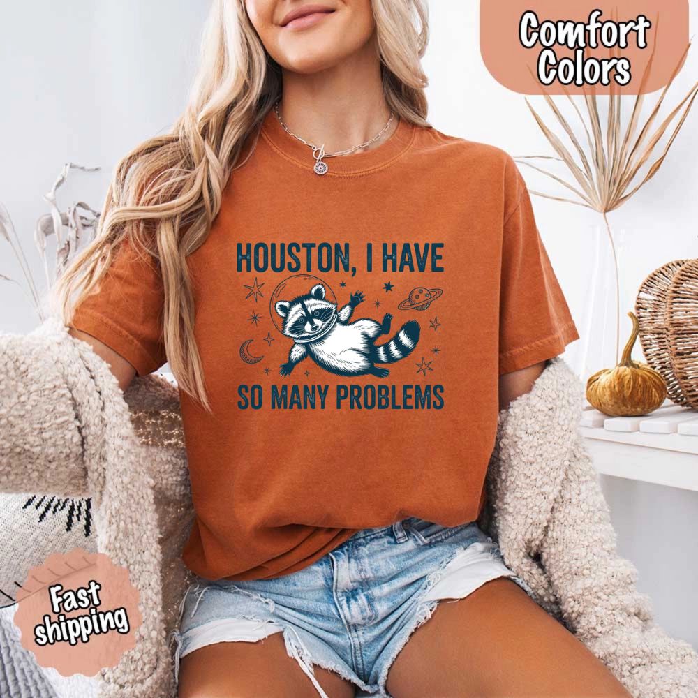 Houston I Have So Many Problems Raccoon Comfort Colors T-Shirts featuring a space-themed raccoon design worn by a woman.