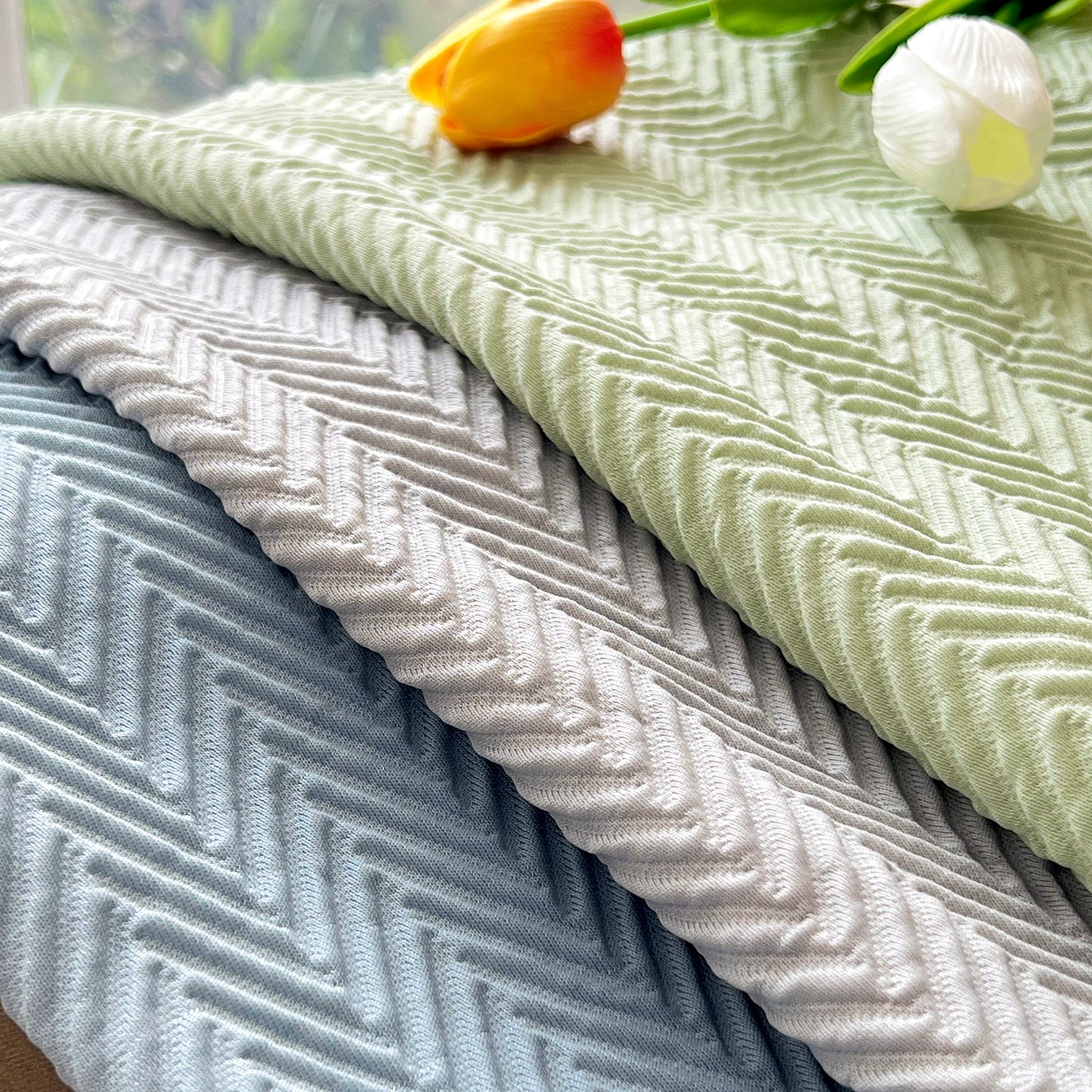 Textured fabric in soft green, blue, and white hues with a zigzag pattern, adorned with orange and white tulips.