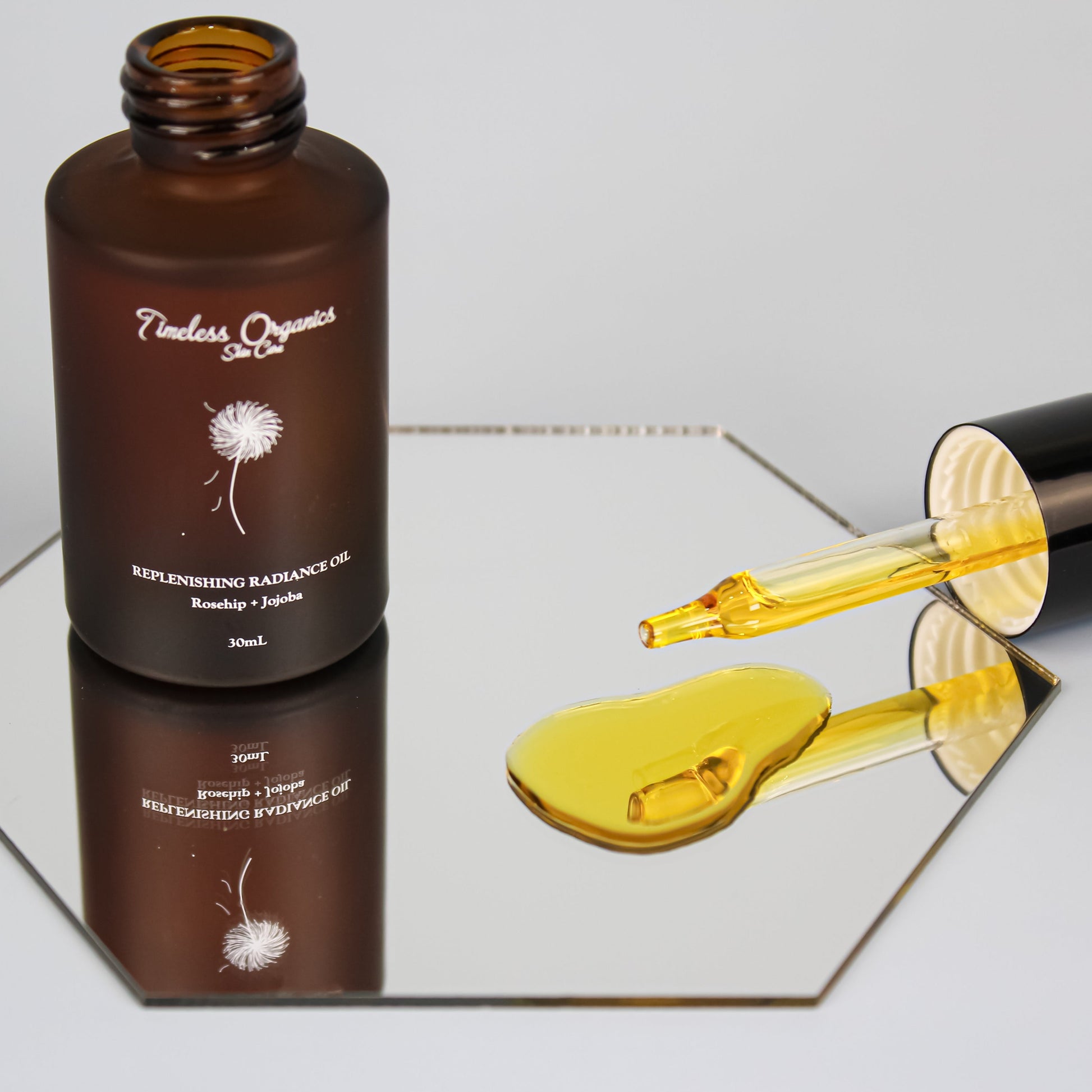 Replenishing Radiance Oil with dropper on reflective surface, showcasing nourishing organic blend for skincare.