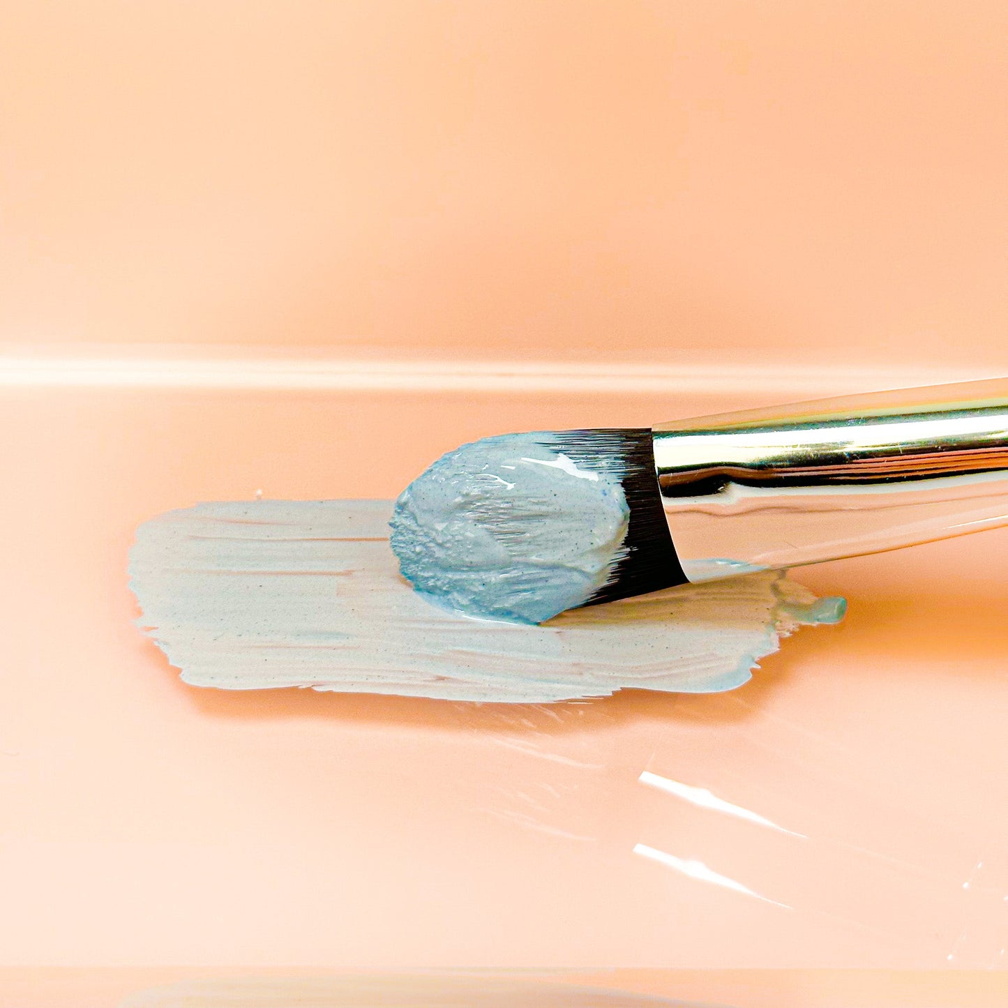 Brush applying Tightening Clay Mask on peach background for skin toning and refining