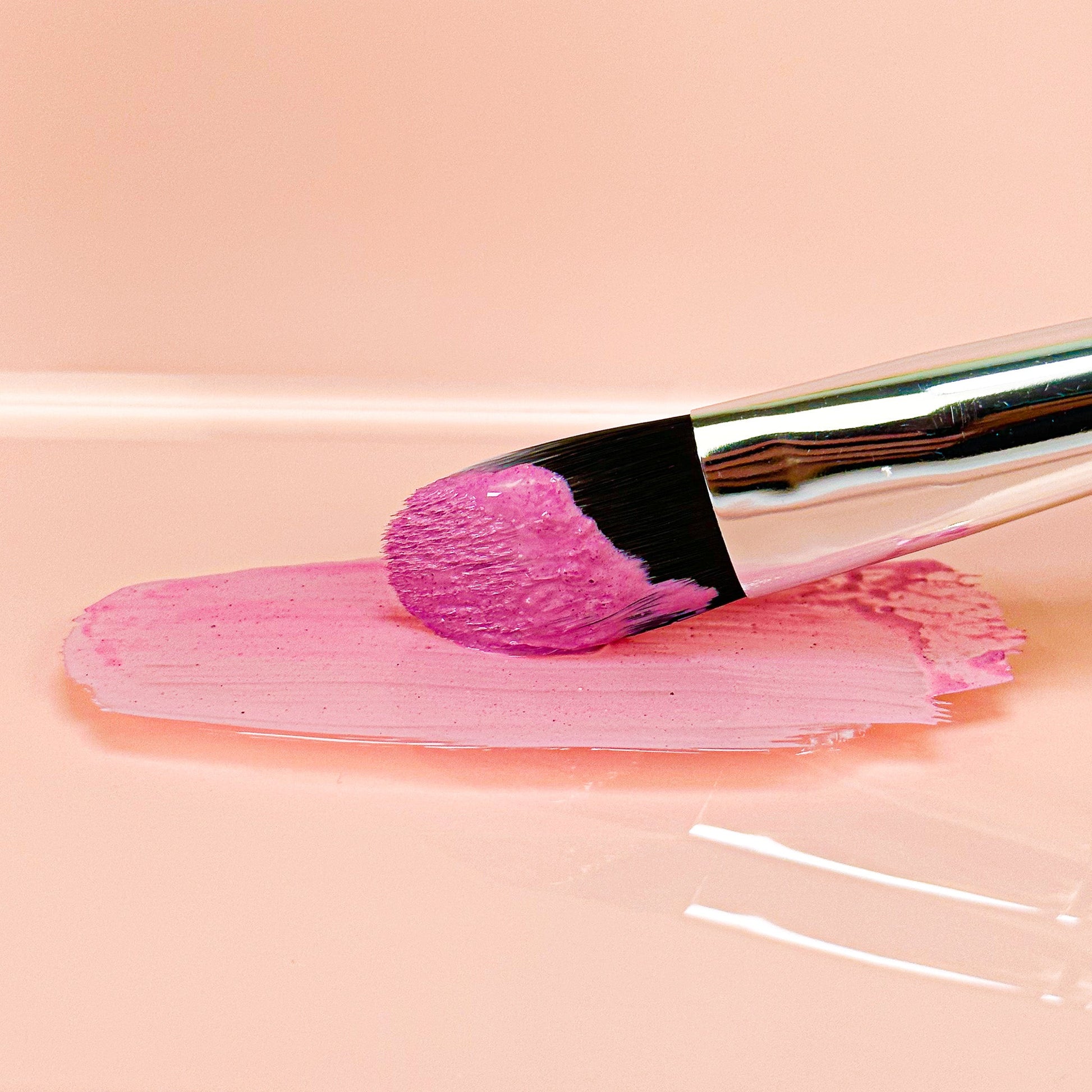 Brush applying pink Brightening Clay Mask to smooth surface, showcasing calm and revitalizing skincare benefits.
