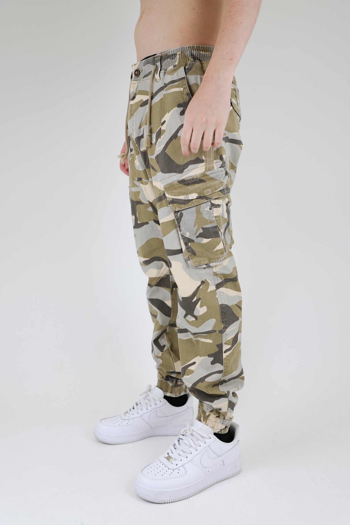 Model wearing AR1001 LIGHT CAMO CARGO JOGGERS with relaxed fit, cargo pockets, and elastic leg openings. Ideal for casual wear and flexibility.