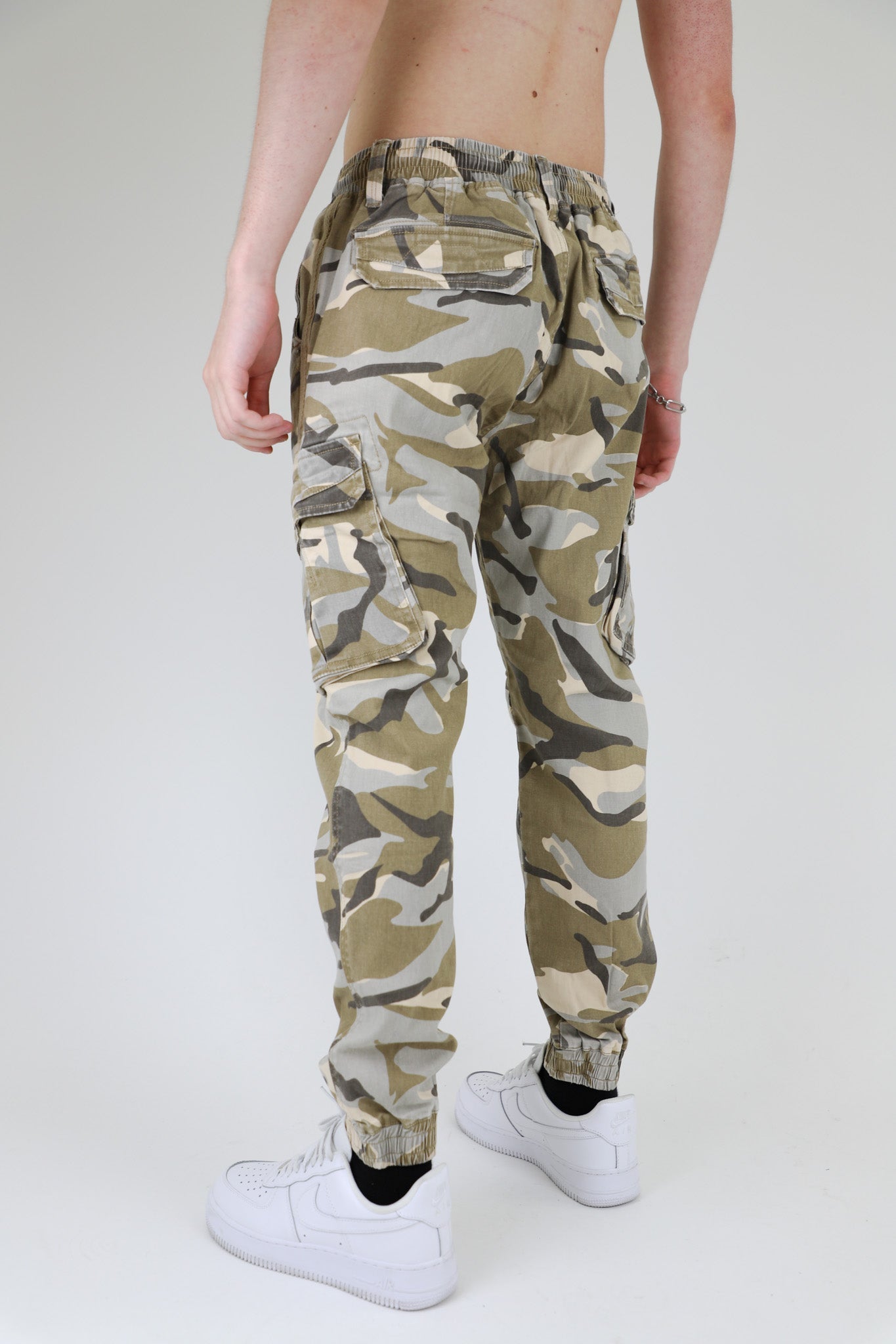 Back view of AR1001 LIGHT CAMO CARGO JOGGERS with side seam pockets, elastic leg openings, and cinch-able waistband, worn by a model.