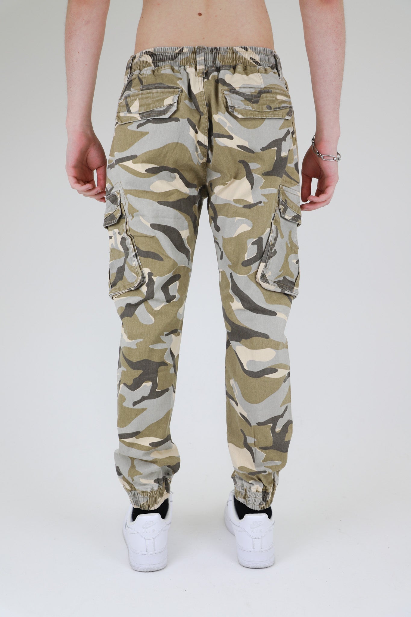Back view of AR1001 LIGHT CAMO CARGO JOGGERS with cargo pockets, elastic leg openings, and camo pattern, worn by model with white shoes.