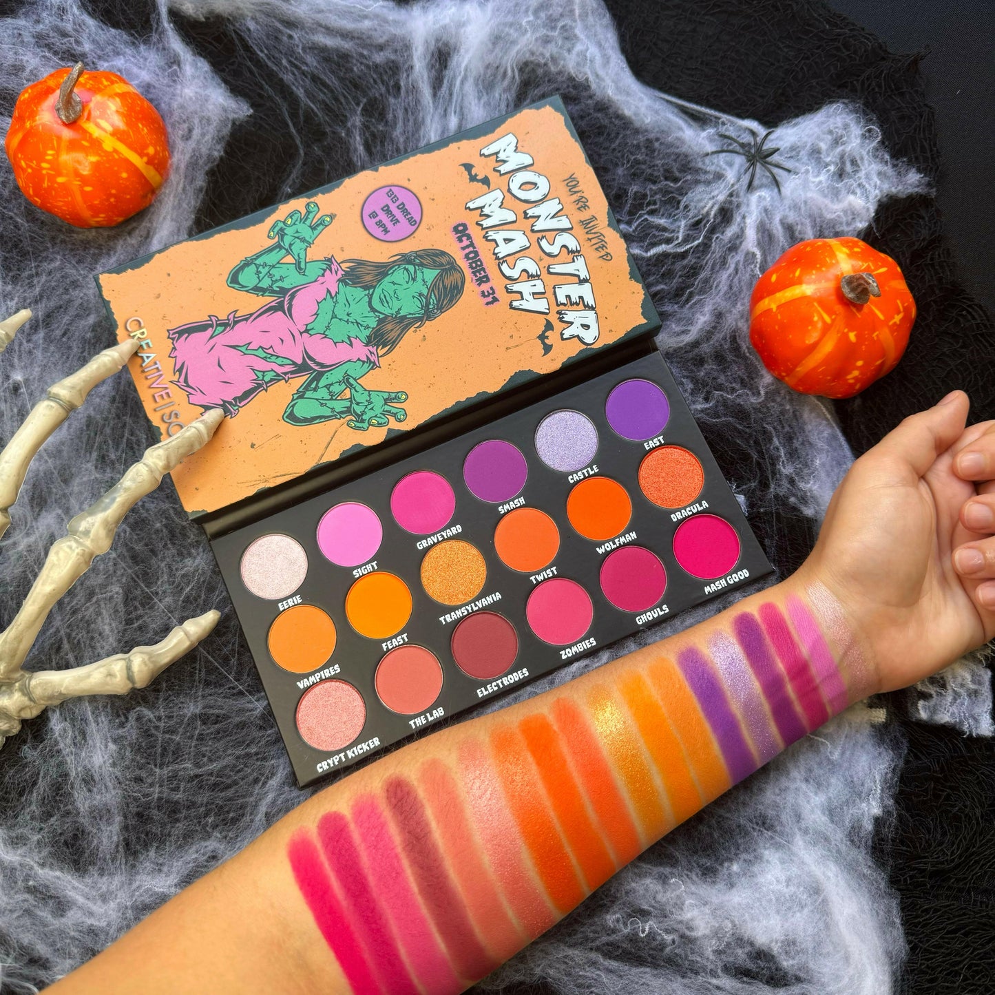 Monster Mash Eyeshadow Palette with 18 vibrant Halloween shades including pinks, oranges, purples, and lavenders displayed on arm.