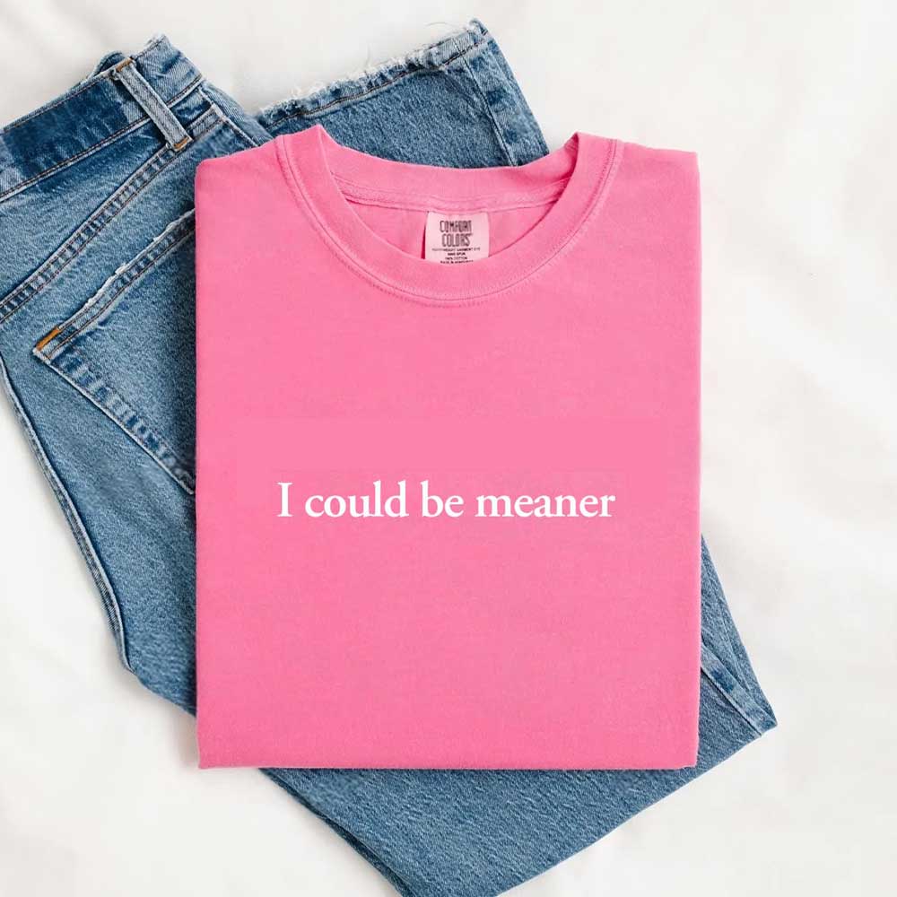 I Could Be Meaner Funny Sarcastic Tee in pink, folded on denim jeans, trendy streetwear for a bold, edgy look.