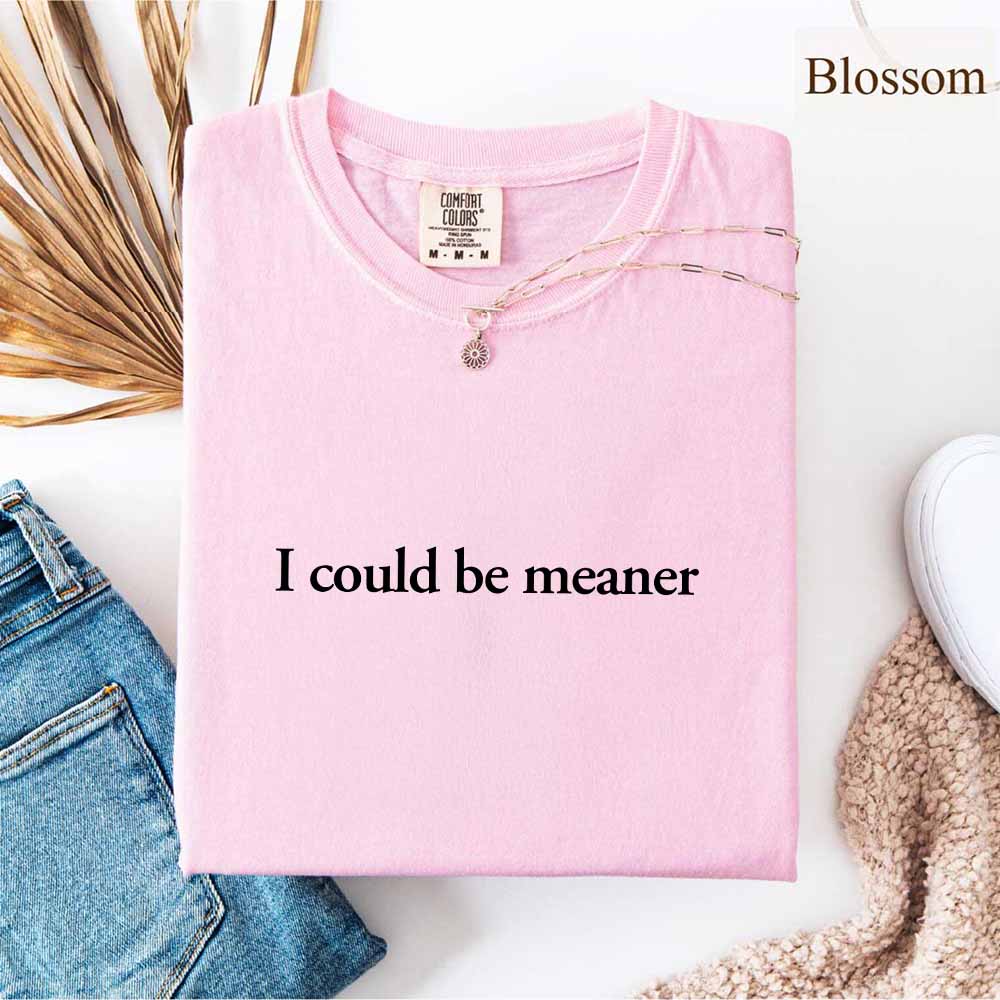 I Could Be Meaner Funny Sarcastic Tee folded with necklace on pink fabric, trendy streetwear design.
