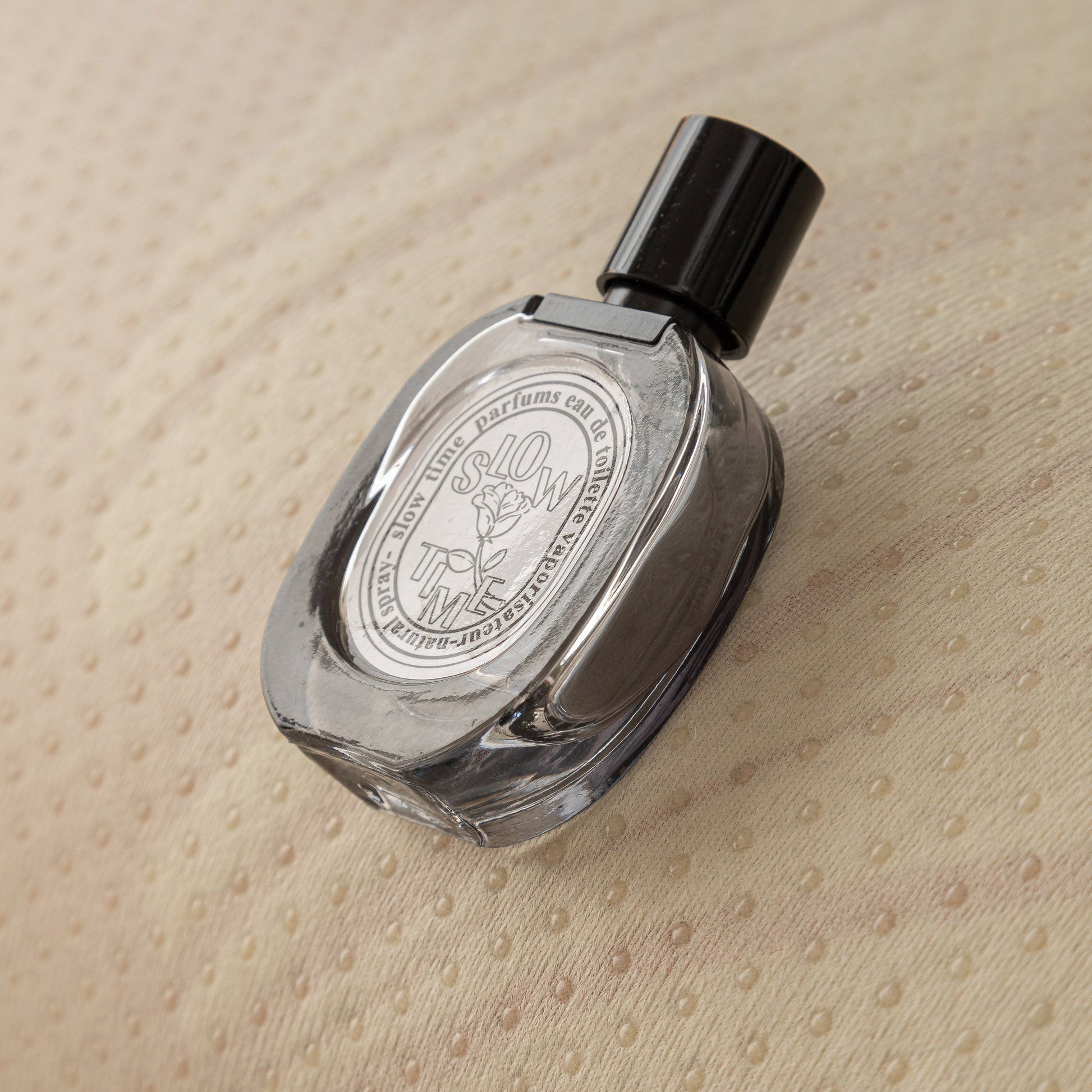 Perfume bottle with black cap on textured beige fabric background