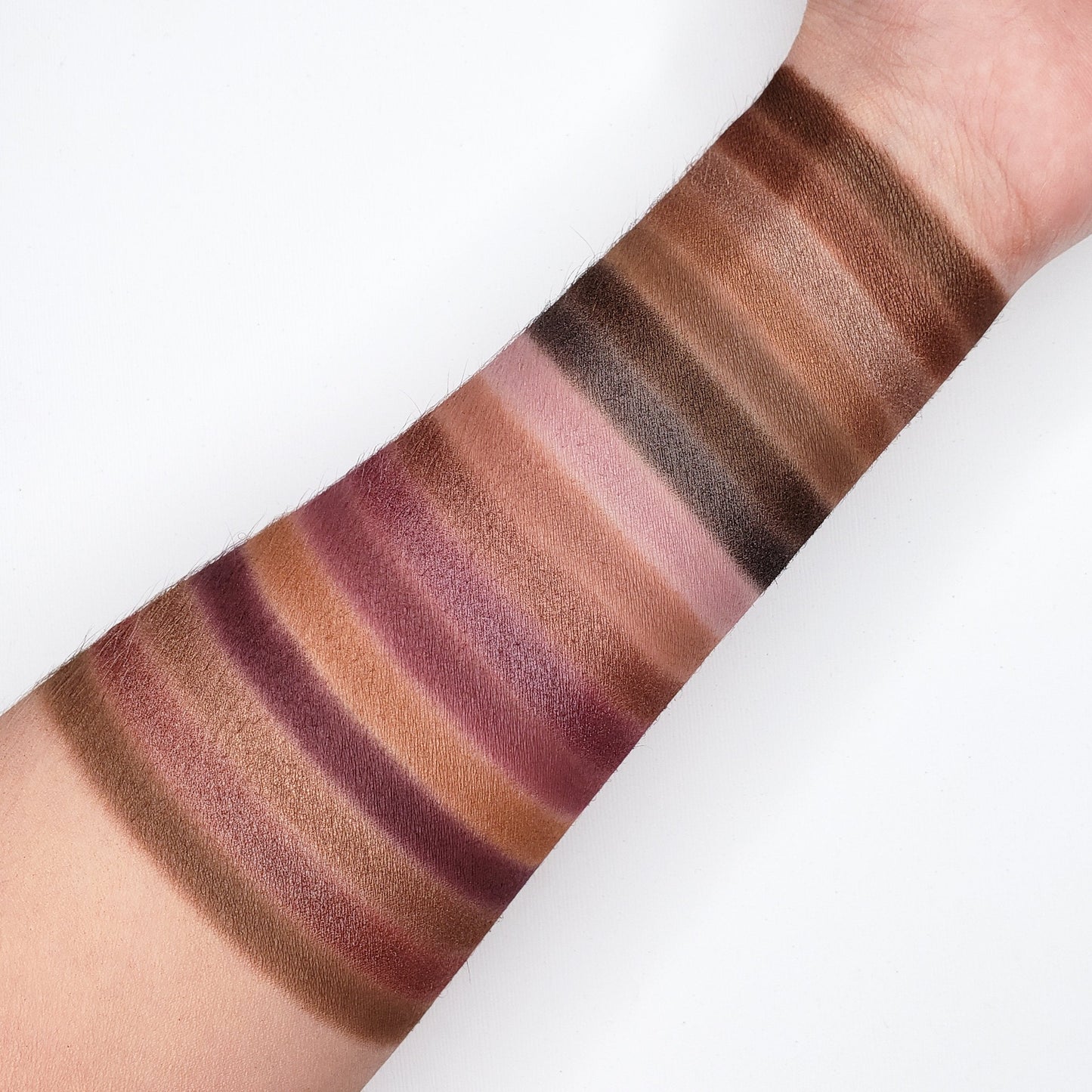 Swatches of warm brown, gold, and mauve shades from JAVA EYESHADOW PALETTE 35J showcasing matte and shimmer finishes on an arm.
