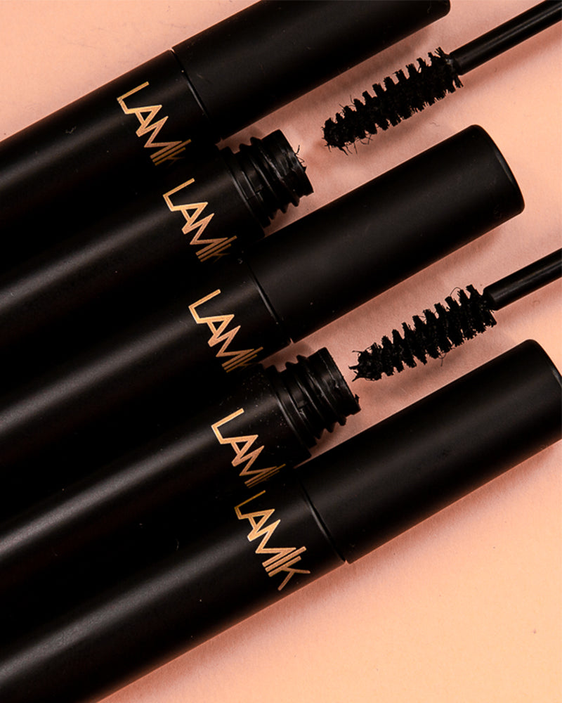 LAMIK Beauty Show Out Mascara in black tubes with applicator brushes displayed on peach background.