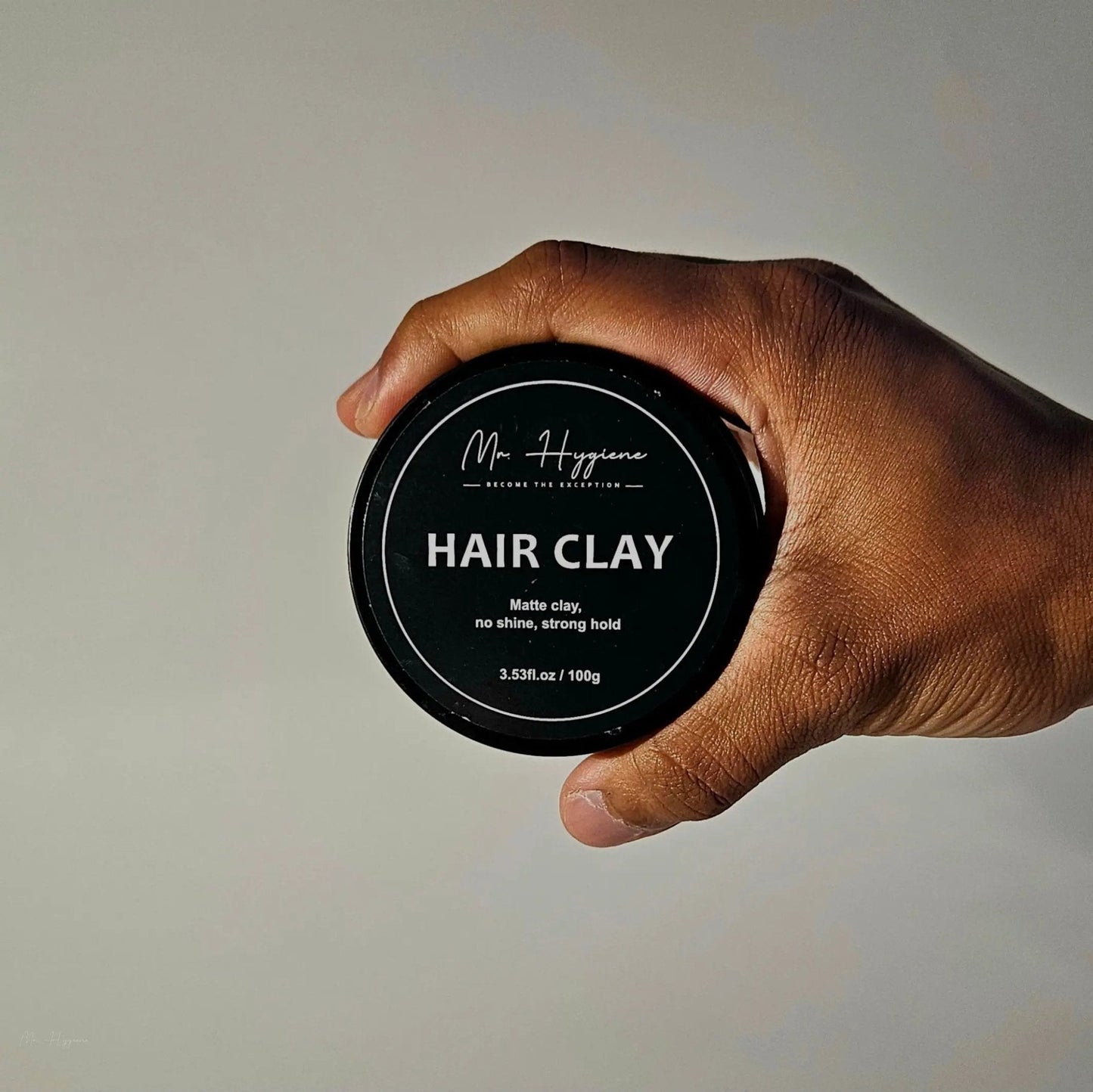 Hand holding Matte Finish Hair Clay - Strong Hold. Zero Shine. All-Day Control. in black circular container.