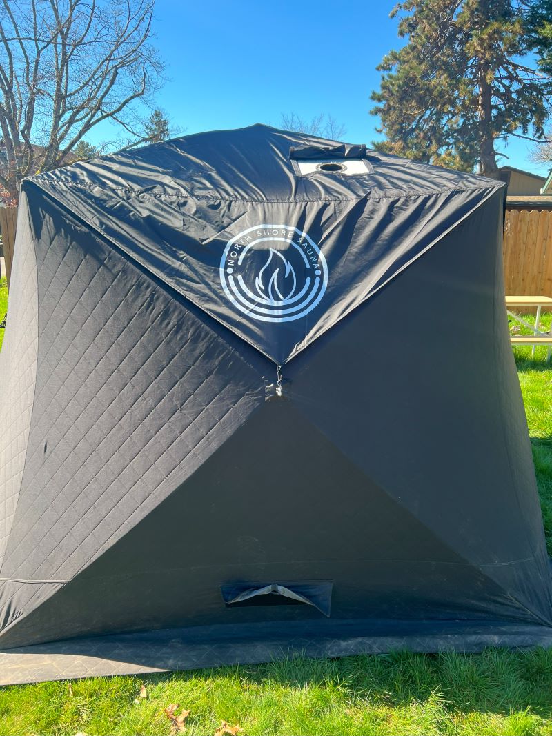 Nova 6 Sauna Tent Rain Cover protecting a black sauna tent in a grassy backyard