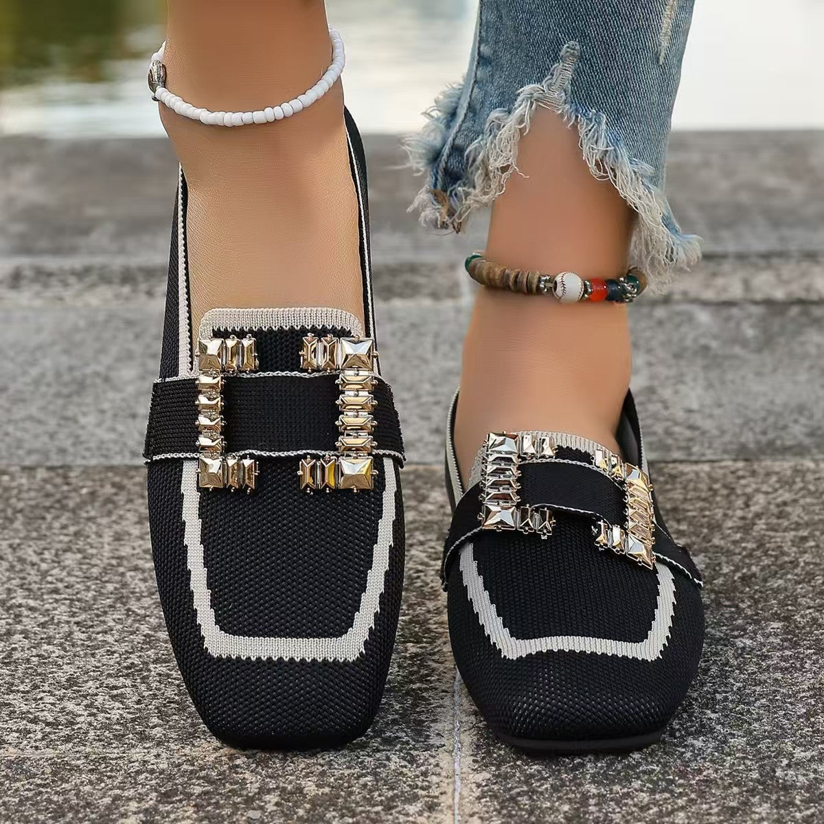 Stylish black loafers with decorative buckles and white trim, worn on pavement with anklets.