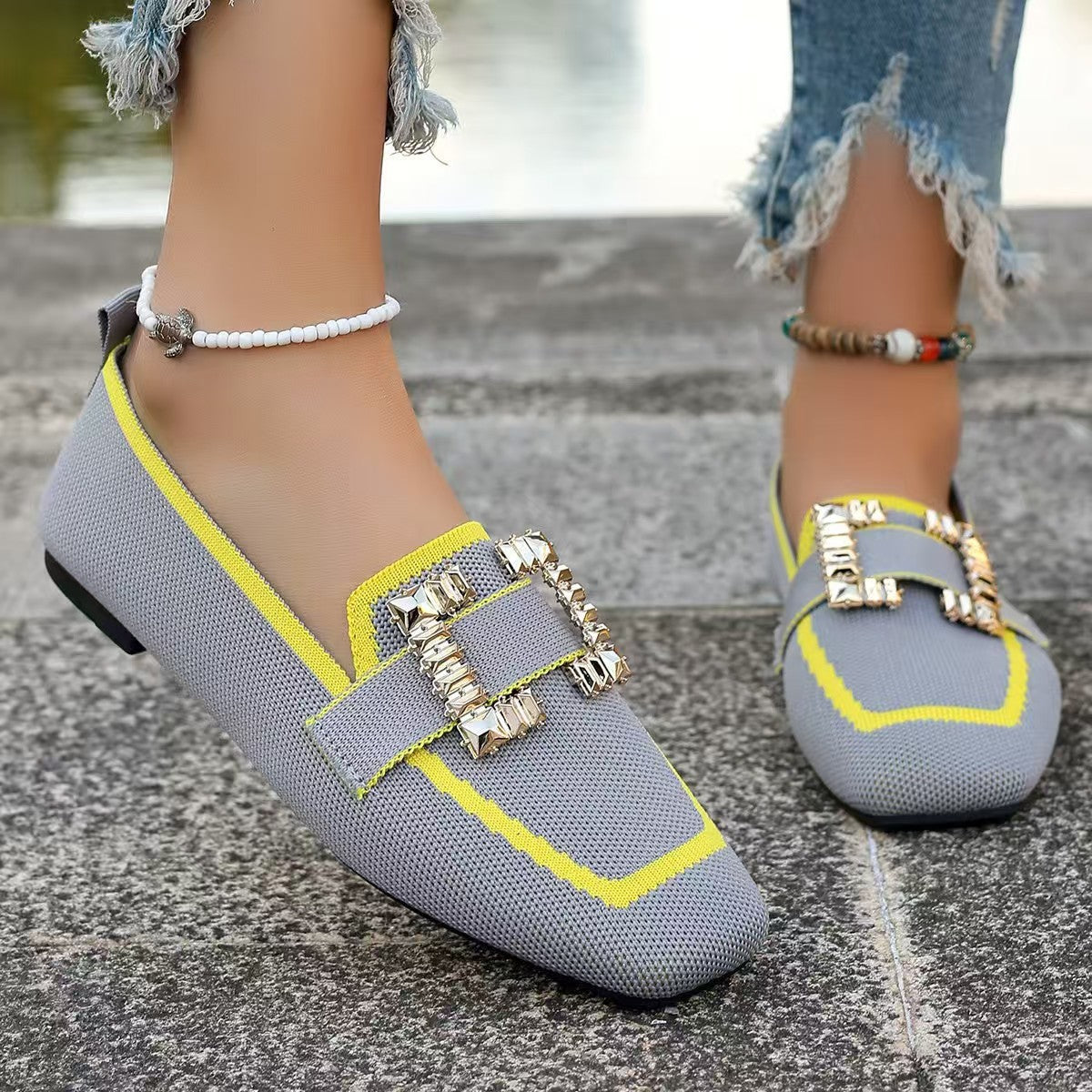Stylish gray loafers with yellow accents and gold buckle detail on pavement.
