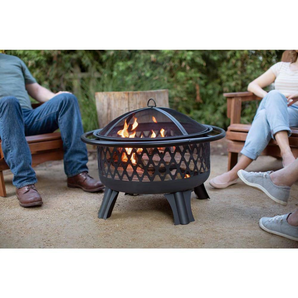 30-inch Black Steel Outdoor Fire Pit Grill with Screen and Poker providing warmth and grilling option, shown on a patio with people.