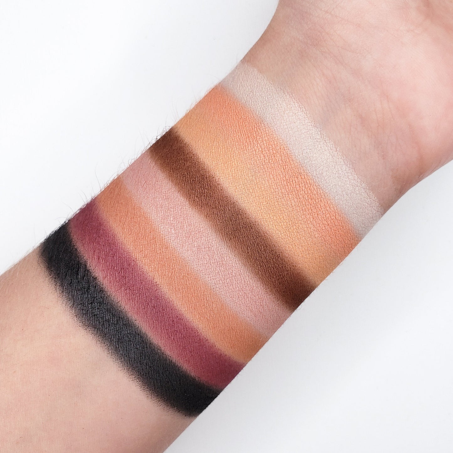 Arm displaying swatches from the GOLDEN PEACH EYESHADOW PALETTE CP15 with matte and shimmer finishes on a light skin tone.