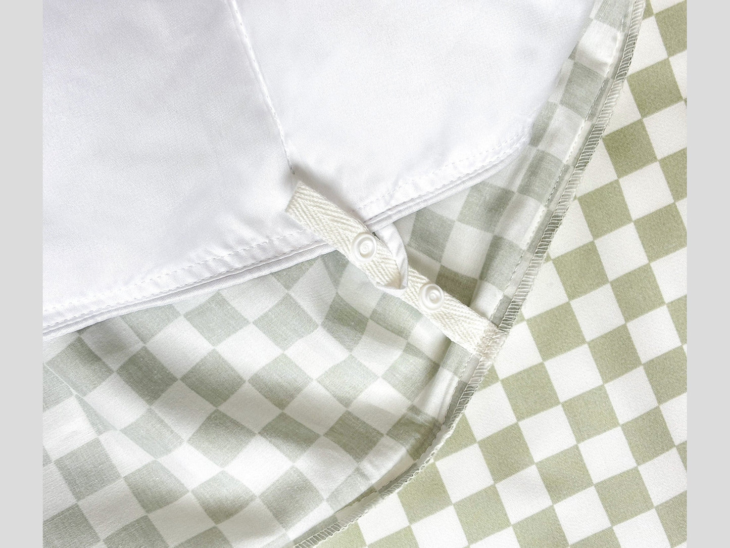 Close-up of SHNUGGLE SNAP-EZ Quilt showing snap-on loops on checkered bedding, highlighting easy attachment and cozy design.