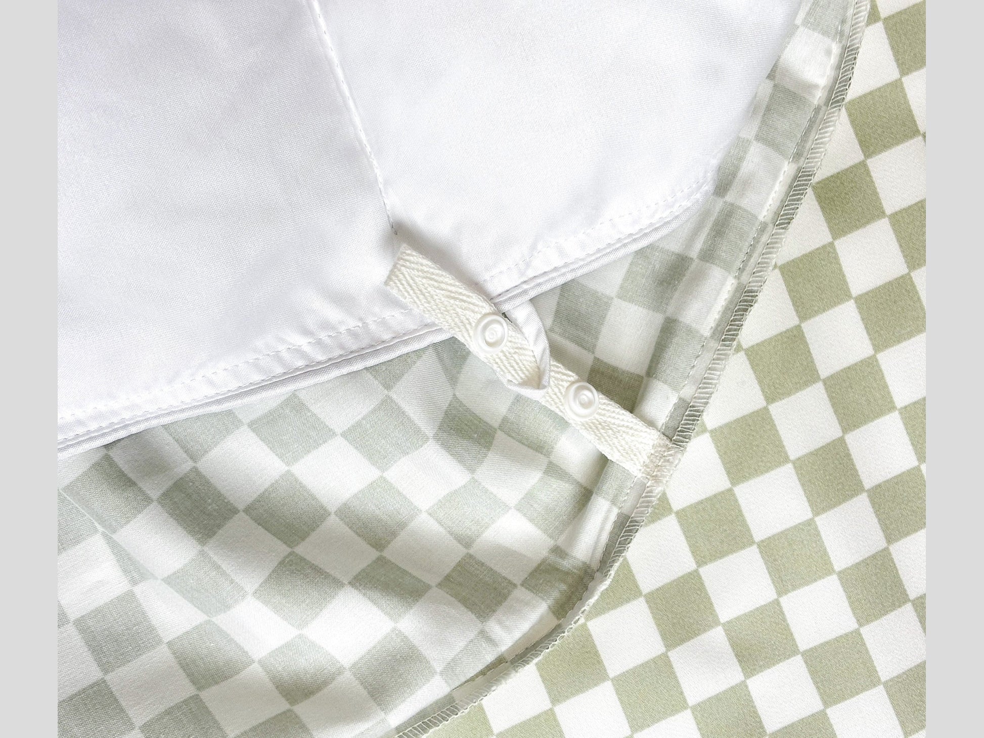 Close-up of SHNUGGLE SNAP-EZ Quilt showing snap-on loops on checkered bedding, highlighting easy attachment and cozy design.