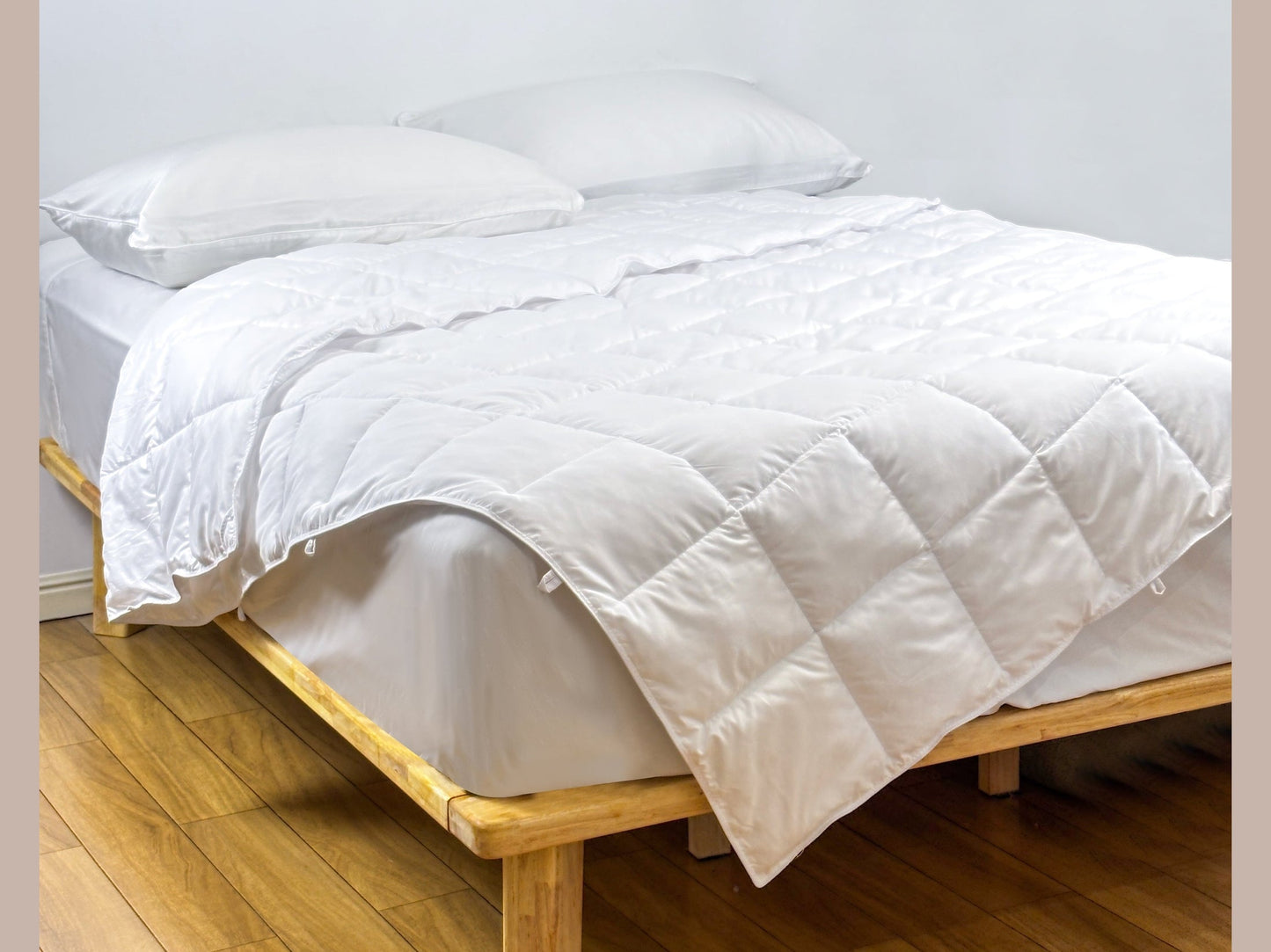 White SHNUGGLE SNAP-EZ Quilt on a wooden bed, showcasing snap-on loops for easy attachment. Soft, lightweight, and dryer-safe.