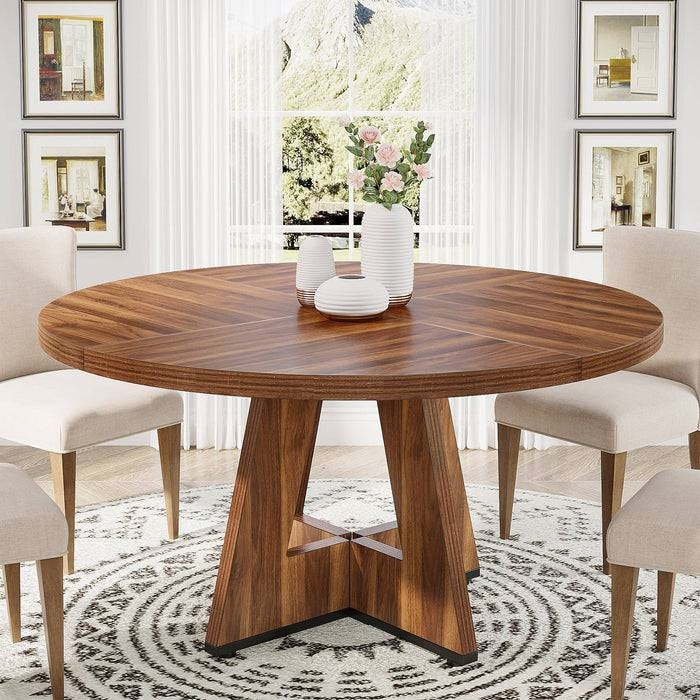 Farmhouse 47-inch Round Kitchen Dining Table in Vintage Brown Wood Finish with decorative items on top, surrounded by chairs in a bright room.