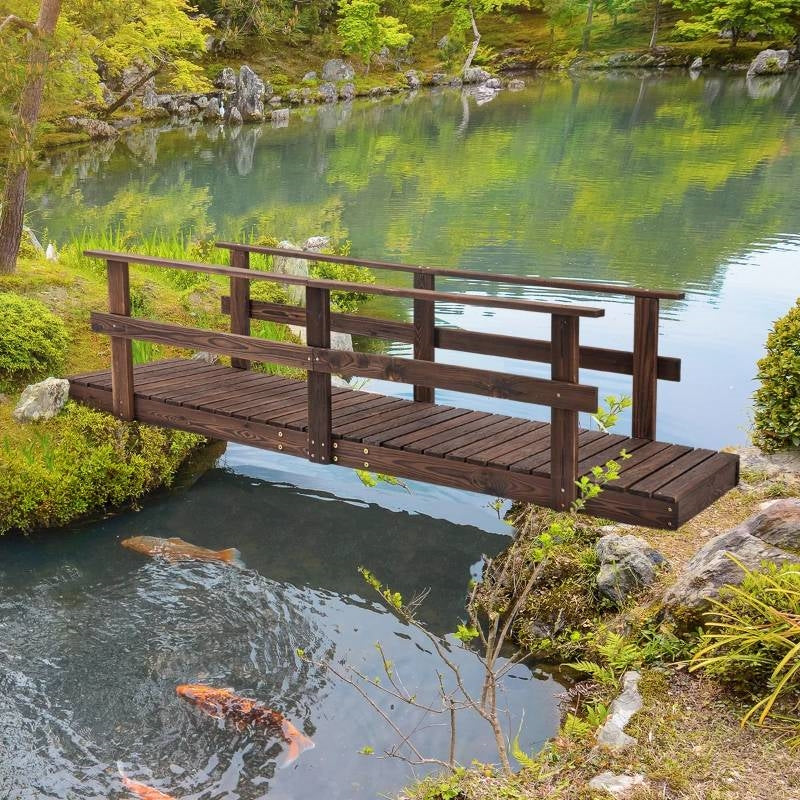 7 ft. Outdoor Wooden Garden Bridge with Hand Rails in Carbonized Wood Finish over a pond with koi fish.
