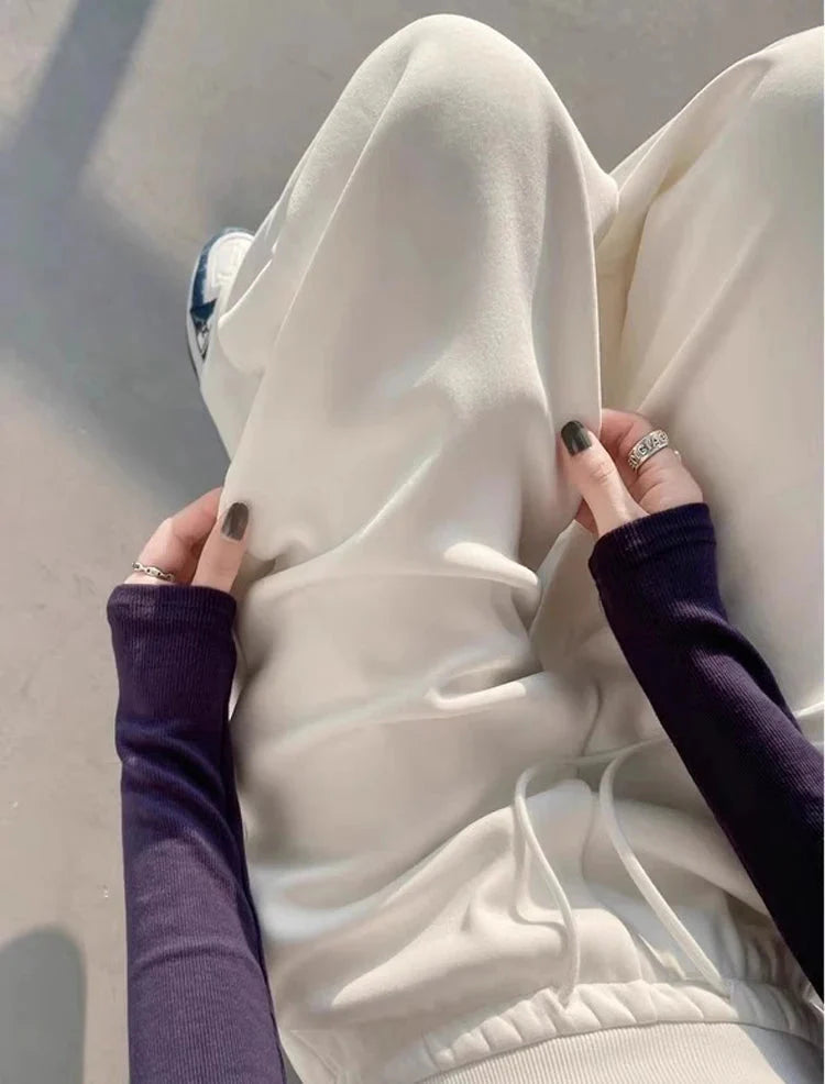 Person wearing white high-waist loose straight pants with long-sleeve top, seated on concrete surface.