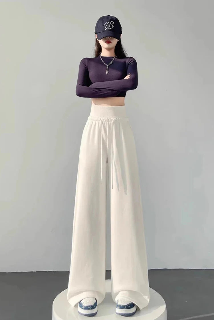 Woman wearing gray high-waist loose wide-leg straight pants with black crop top and cap.