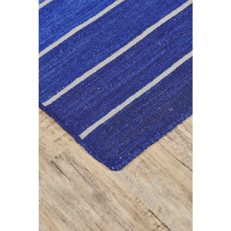 Close-up of 8' x 11' Striped Hand-Tufted Wool/Cotton Blue Area Rug with serape-inspired pattern on wooden floor.