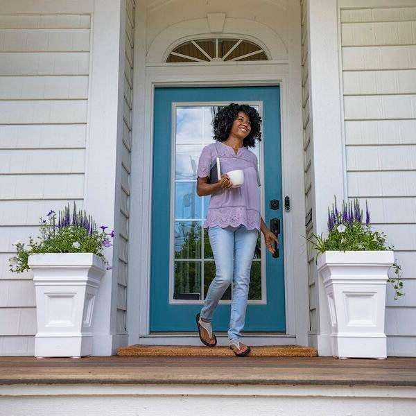 Woman walking past front door with Set of 2 - 24 inch High Self Watering Planter Box in White Plastic Resin on porch