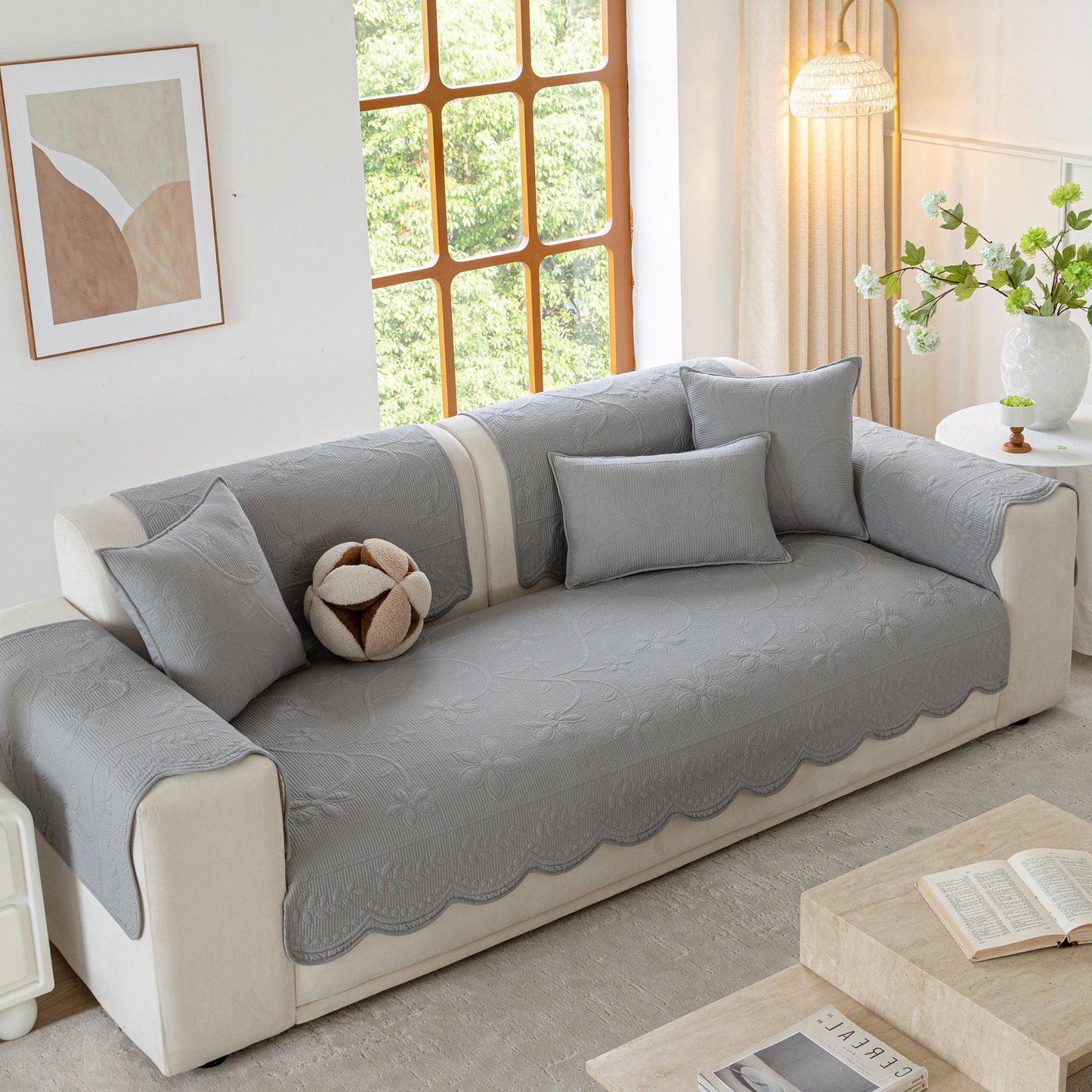Floral Cotton Quilted Sofa Cover, Non-Slip Couch Protector with Scalloped Edges on a sofa with pillows in a bright living room.