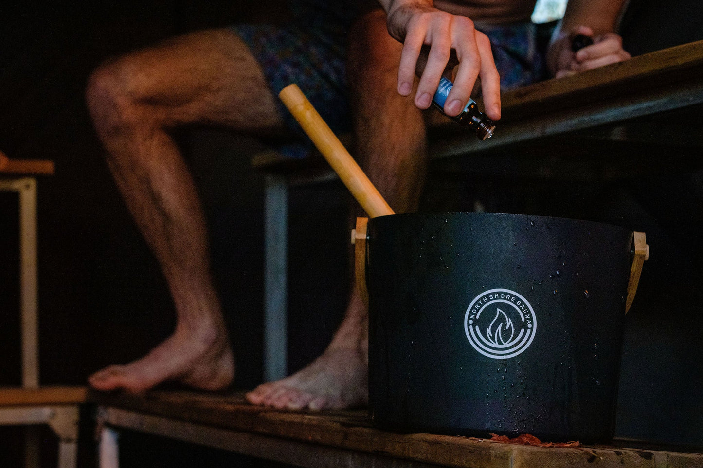 Person adding essential oil blend to sauna bucket | Essential Oil Blend | Sauna In Nature