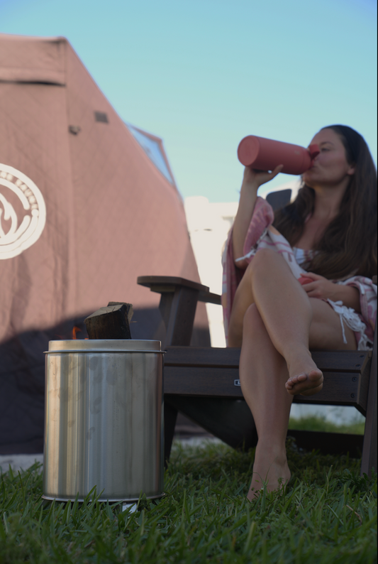 Woman relaxing beside Small Smokeless Fire Pit in outdoor setting, enjoying a drink under clear skies in backyard.
