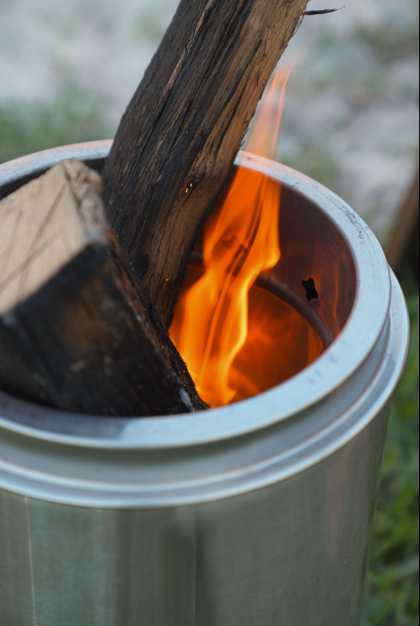Stainless steel small smokeless fire pit with active flame and wood logs, ideal for outdoor relaxation and sauna cool down sessions.