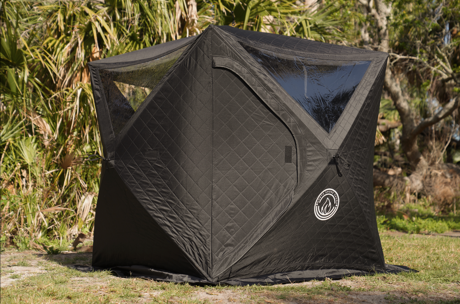 Black Mini Cube Sauna Tent (2-person; tent only) set up outdoors in a grassy area with surrounding greenery.