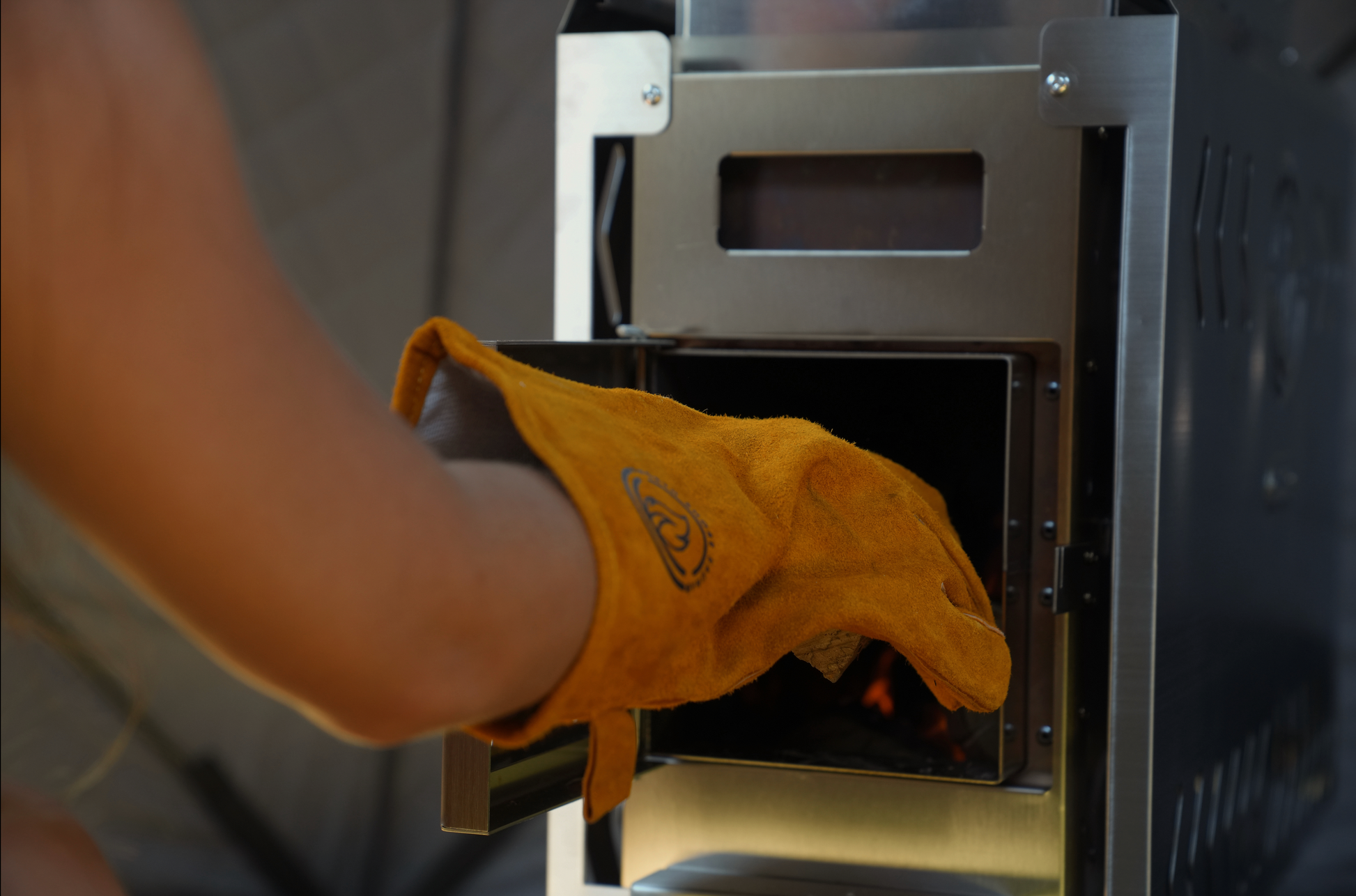 Person using wood-fired stove with gloves in Nova 4 Sauna Tent Premium Package (4-person), featuring stainless-steel design.