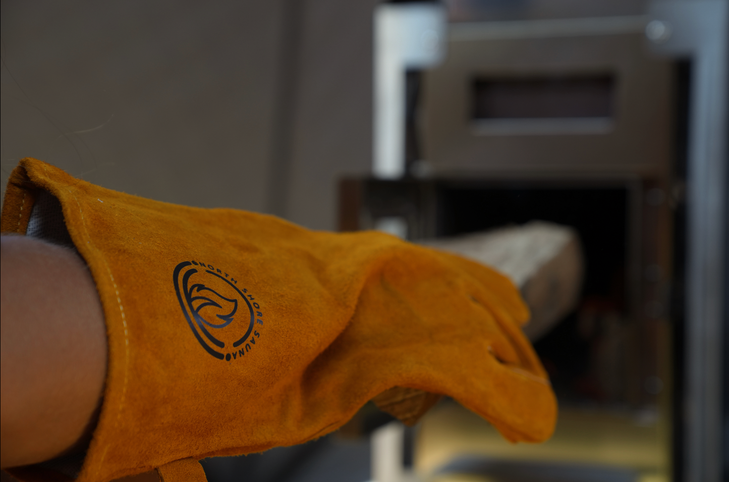 Heat Resistant Leather Gloves handling firewood near sauna stove, ensuring protection and secure grip against intense heat.