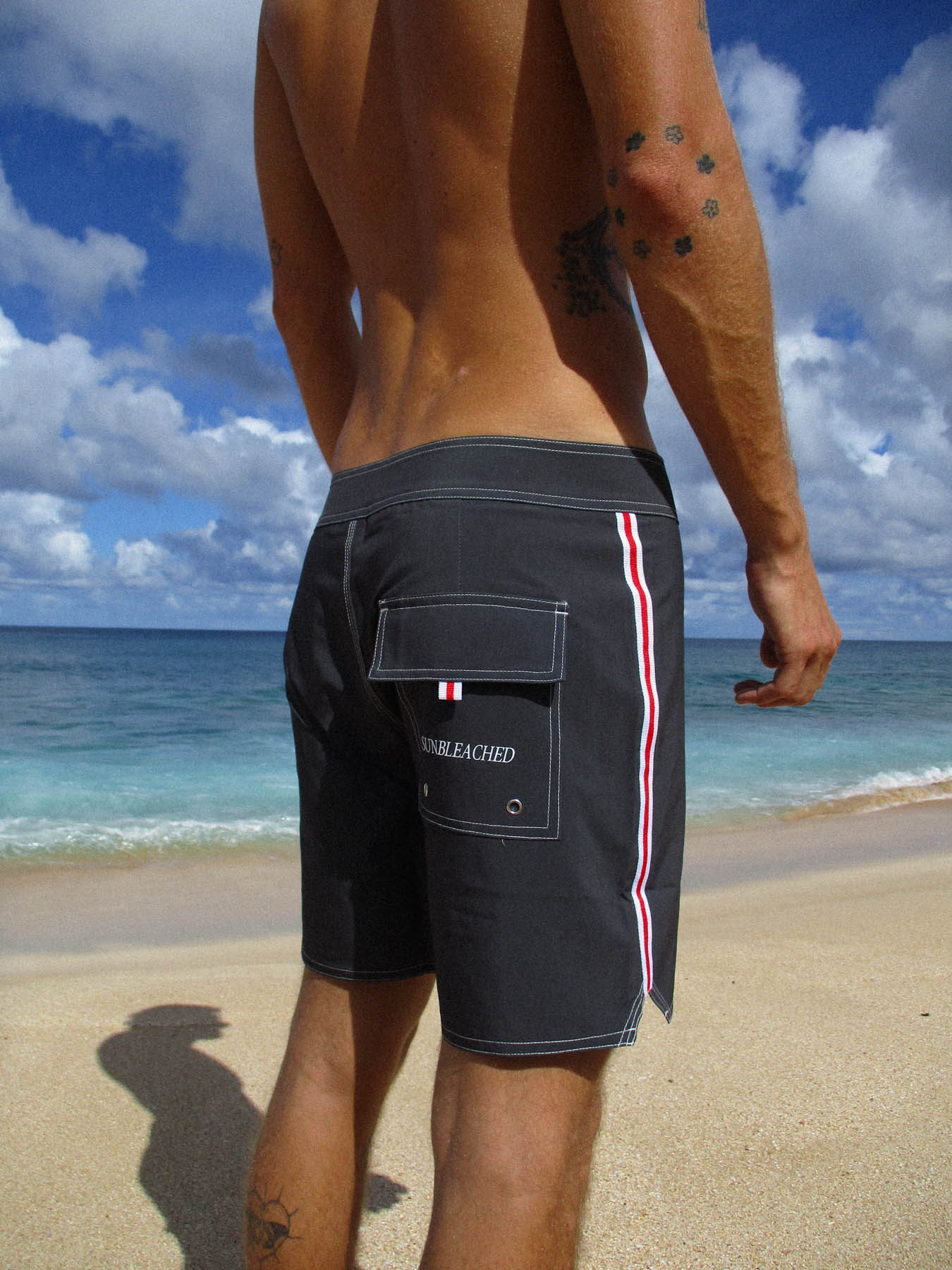 Man wearing the classic boardshort - yards in Pirate Black on a beach, featuring retro style and 4-way stretch dobby fabric.