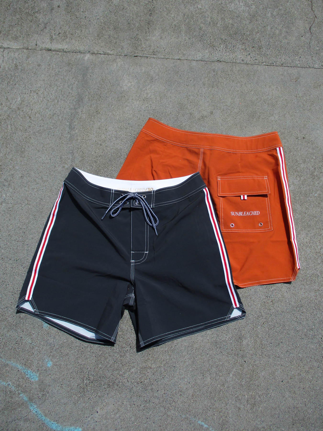 Two pairs of surfer boardshorts with retro design, featuring the classic boardshort - sunset in burnt orange on concrete.