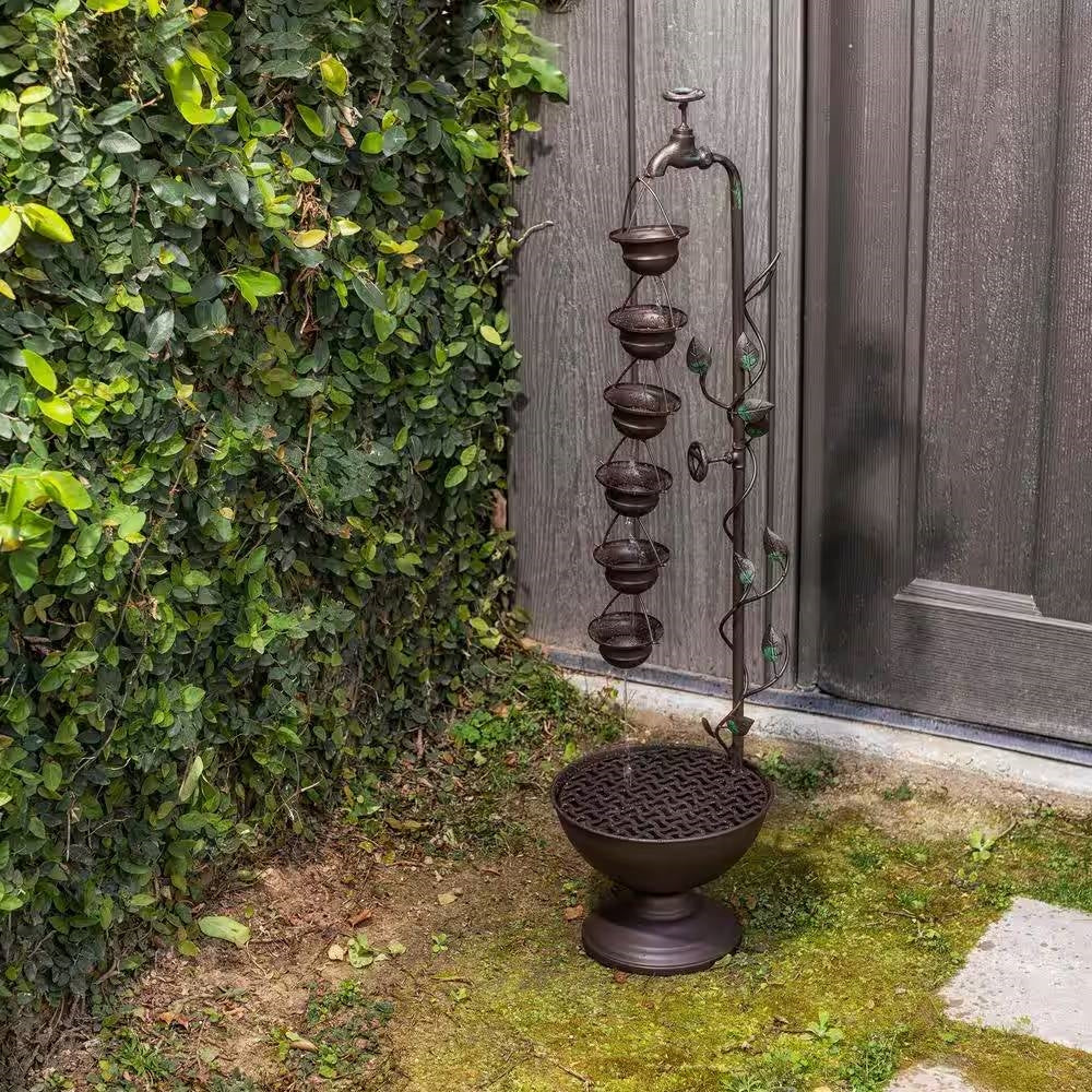 Outdoor Indoor 6-Tier Hanging Cups Water Fountain in Bronze Finish next to greenery, enhancing outdoor decor with vintage charm.