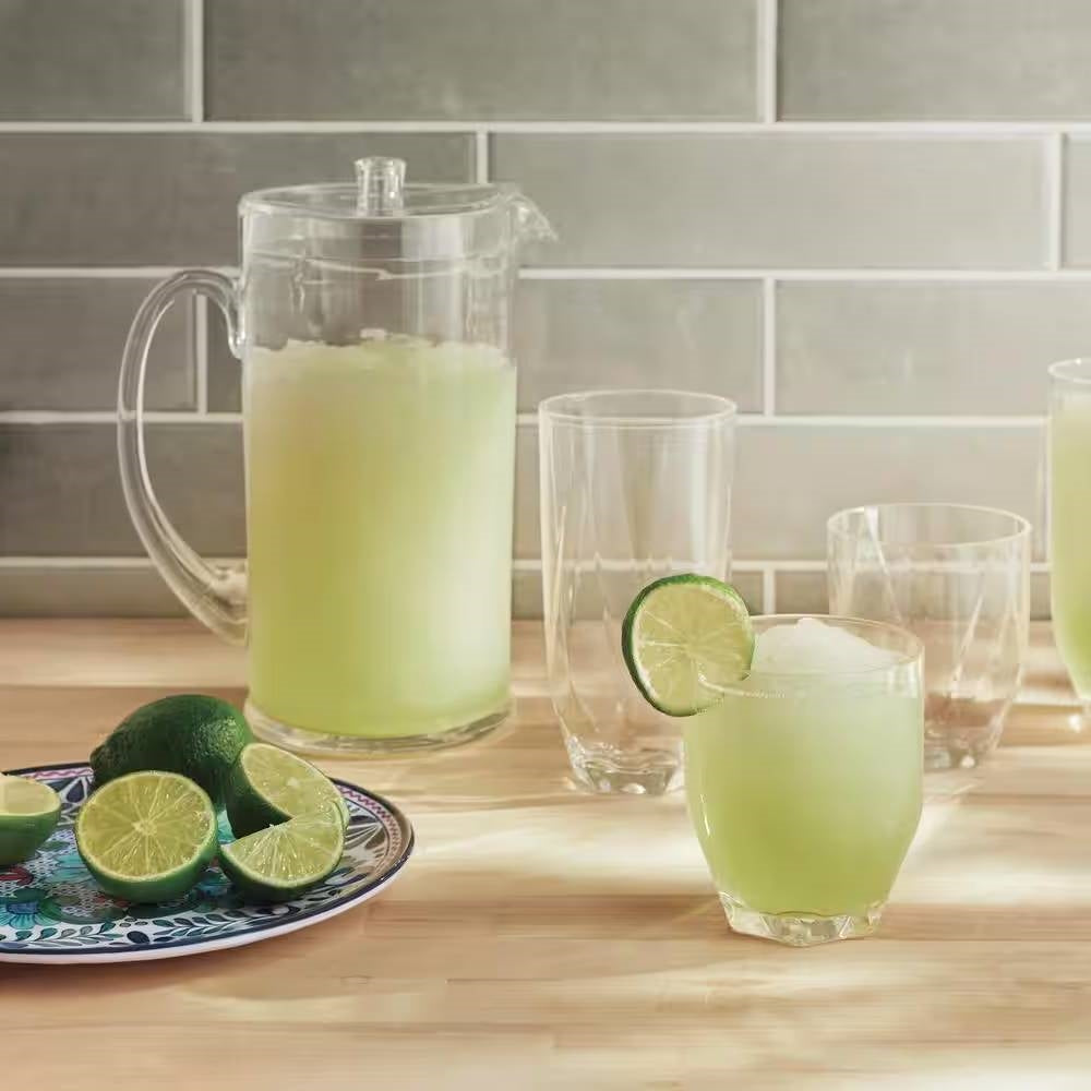 Transparent pitcher and glasses filled with limeade, with sliced limes on a decorative plate, on a wooden countertop.