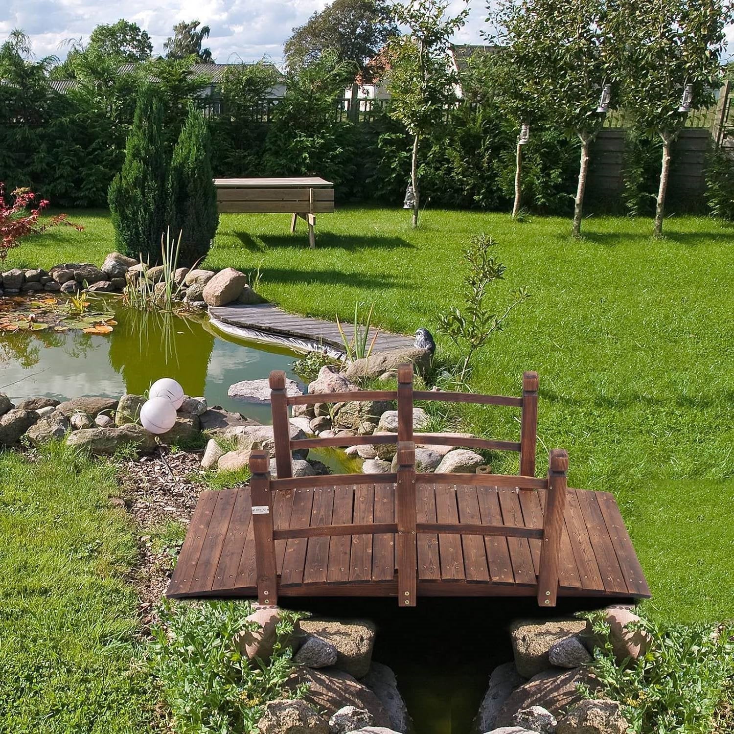 Outdoor 5-foot Solid Fir Wood Garden Bridge in Rustic Brown Finish over a garden pond, enhancing landscape with natural beauty.