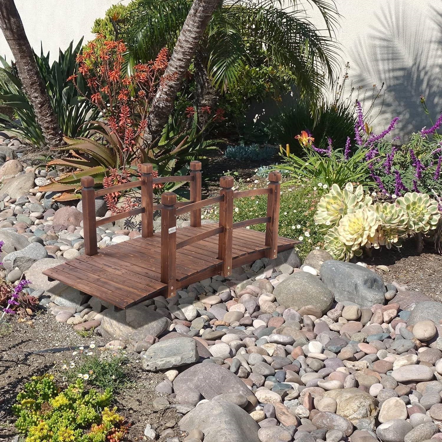 Outdoor 5-foot Solid Fir Wood Garden Bridge in Rustic Brown Finish over decorative garden rocks and plants.