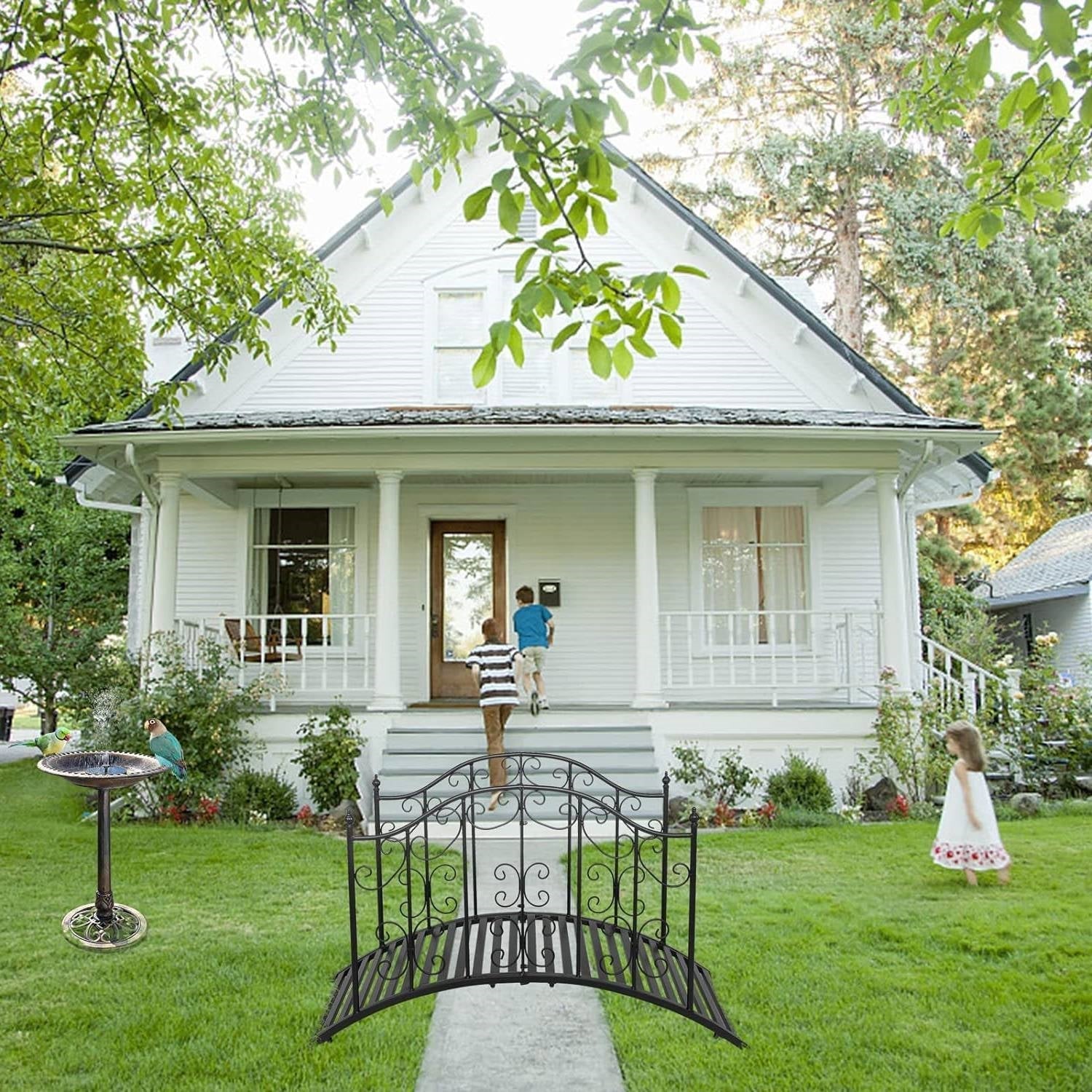 Sturdy Outdoor Rust-Proof 4-Foot Black Metal Arch Garden Bridge decorates a classic white house lawn with children playing.