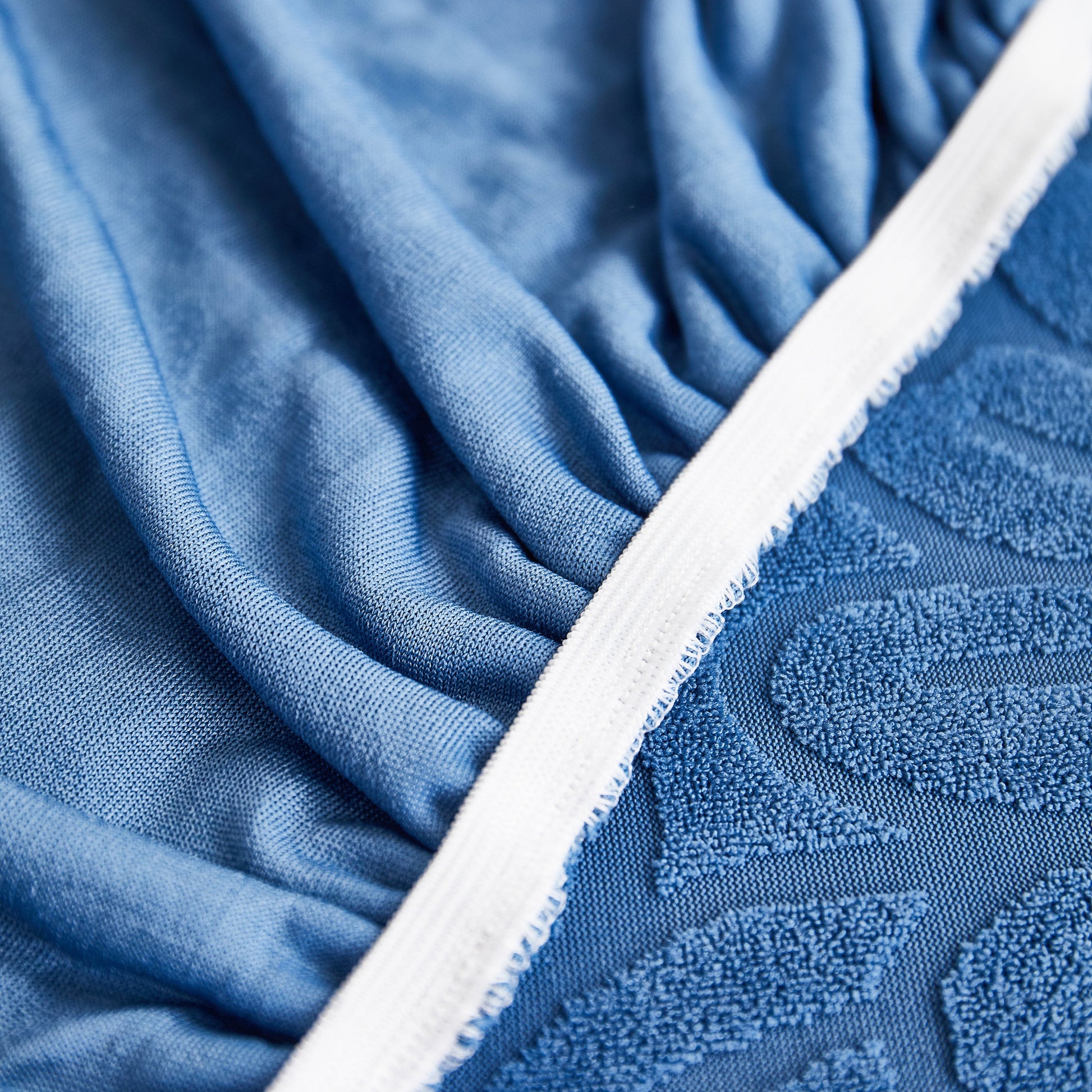 Close-up of sunflower-patterned elastic skirted sofa seat cover in blue tone, highlighting jacquard chenille fabric texture and quality stitching.