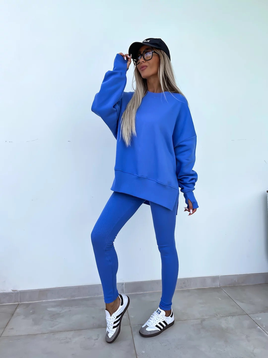 Woman wearing a Women's Casual Sweater Suit – Loose Split Top & Fitted Trousers Set in blue, paired with sporty shoes and a cap.