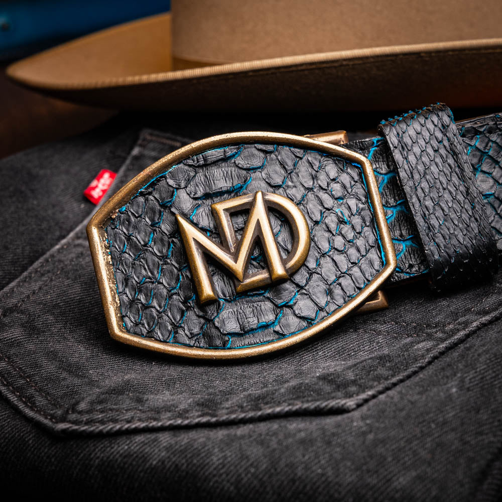 Close-up of Arkansas Belt Black / Blue with genuine python skin and antique brass buckle on a dark fabric background.