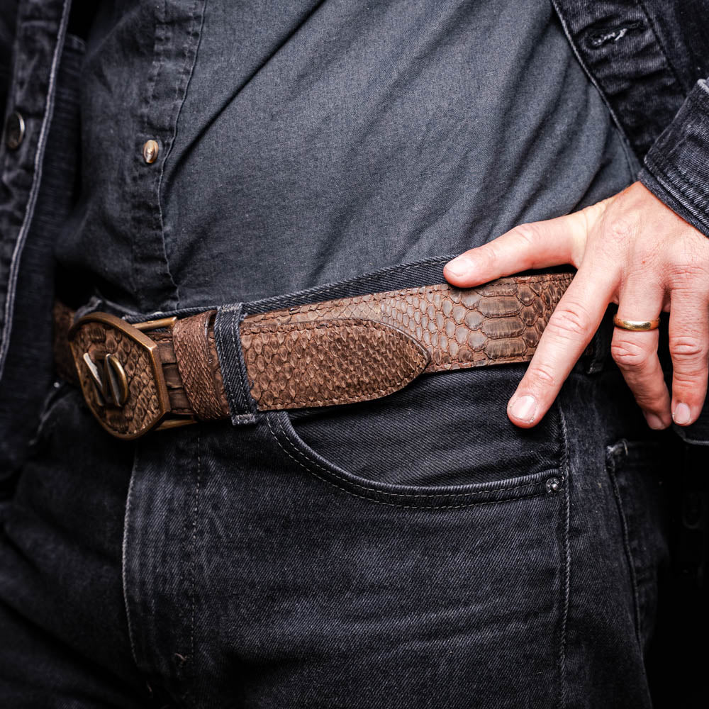 Close-up of a person wearing the Arkansas Belt Brown, made from genuine python skin with antique brass buckle, showcasing Western style.