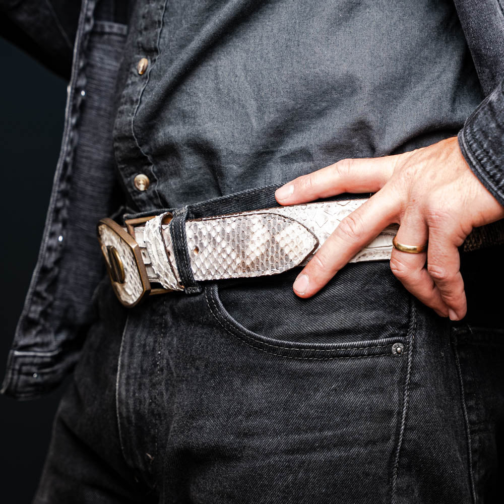 Arkansas Belt Natural featuring genuine python skin with a Western-style antique brass buckle, worn with casual jeans.